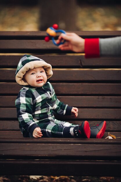 Adorable baby in warm overall with hood sitting on foliage