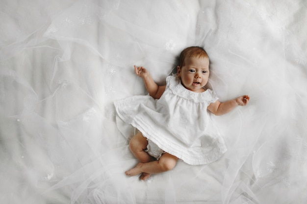 白いドレスを着たかわいい赤ちゃんがベッドにあります。
