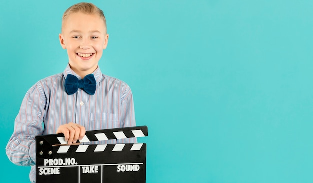 Adorable boy holding clapperboard copy space