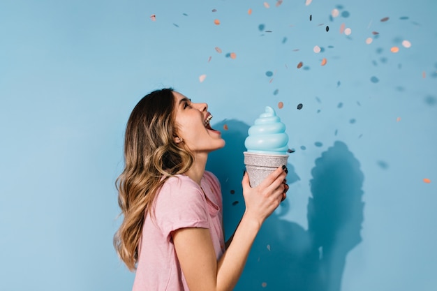 아이스크림 파란색 벽에 포즈를 취하는 귀여운 갈색 머리 여자