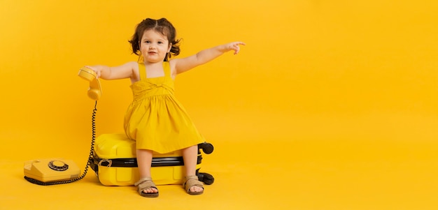 Adorable child posing with telephone and luggage