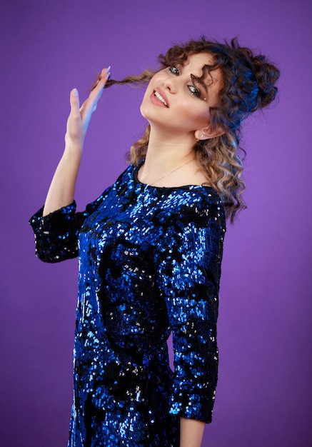 Adorable curlyhaired girl stretching her hair and standing on purple background High quality photo