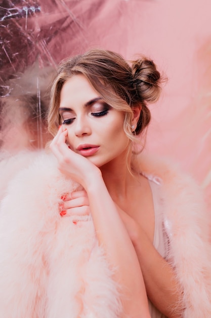 Adorable cute girl with bunch hairstyle dreamy posing and gently touching her face. Pretty young curly woman in fluffy outfit standing in front of glitter background with eyes closed