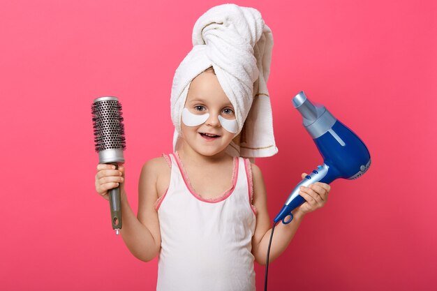 Adorable female child holding hair dryer and comb in hands