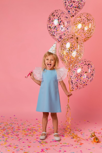 Adorable girl in costume with balloons and party hat