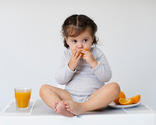 Adorable girl eating orange and looking away