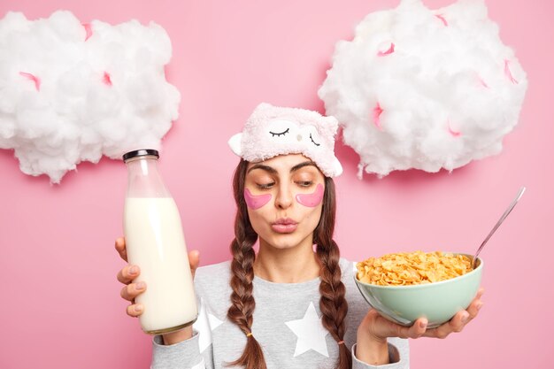 Adorable girl has two pigtails keeps lips folded looks at cornflakes