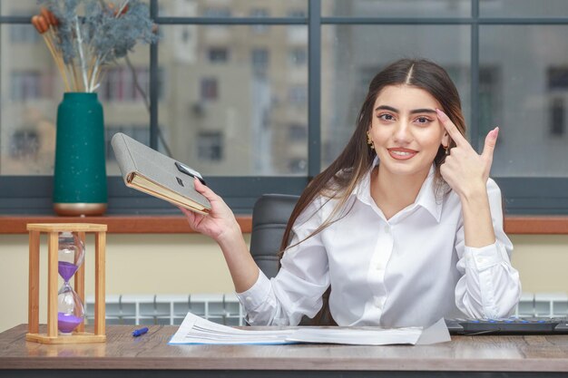 Adorable girl holding her notebook and put her finger to her forehead