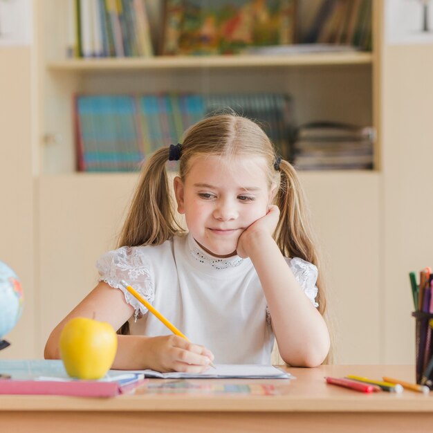 Adorable girl looking at apple during lesson