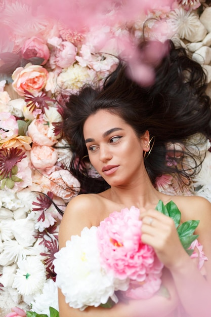 Adorabile ragazza sdraiata su fiori colorati e con in mano un mazzo di fiori foto di alta qualità