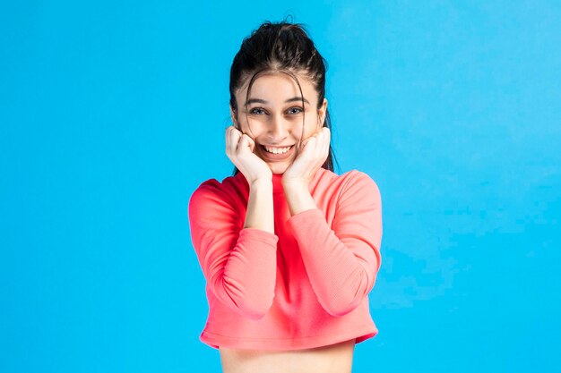 Adorable girl put her hands to her chin and smiling for the camera on blue background High quality photo