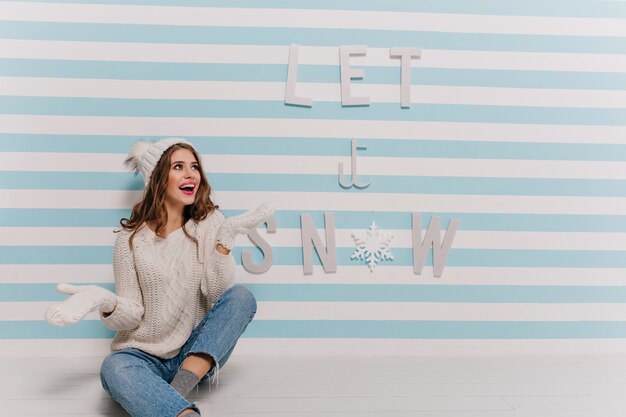 Adorable girl rejoices and enthusiastically poses in wall with winter clothes