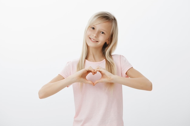 Adorable girl showing heart gesture and smiling