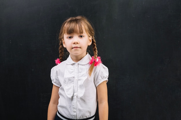 Adorable girl with braids on blackboard