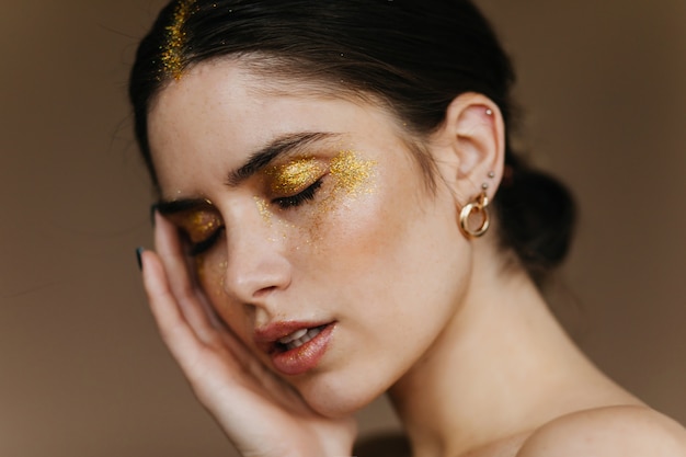 Adorable girl with elegant earrings posing with eyes closed. Close-up portrait of gorgeous brunette woman.