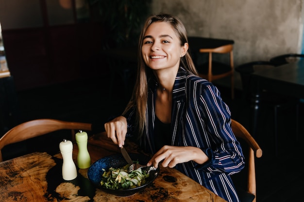 Free photo adorable girl with long hair eating vegetables. laughing refined lady enjoying favorite salad.