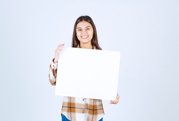 Foto gratuita adorabile ragazza con bianco grande vuoto in posa sul muro bianco.