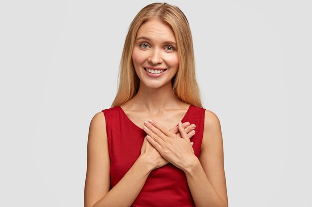 Adorable glad woman keeps both palms on heart, expresses good attitude to someone, has appealing look