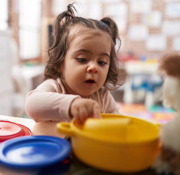 Free photo adorable hispanic girl playing with play kitchen standing at kindergarten