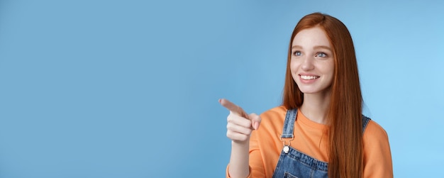 Free photo adorable kind gentle goodlooking redhead girl look pointing left amused smiling astonished sighing