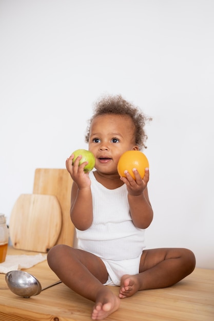 Adorable little black baby holding some fruits