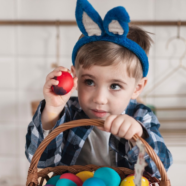 Бесплатное фото Прелестный маленький мальчик держит корзину с пасхальными яйцами