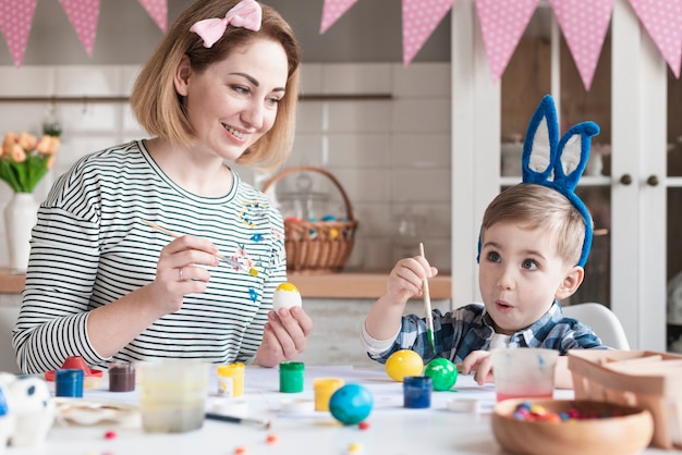 Adorable little boy painting easter eggs with mother