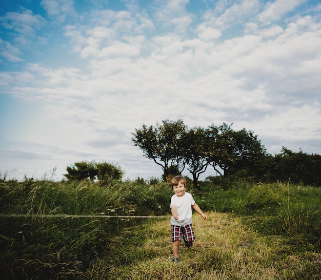 Adorable little boy stands on a green field in the rays of evening