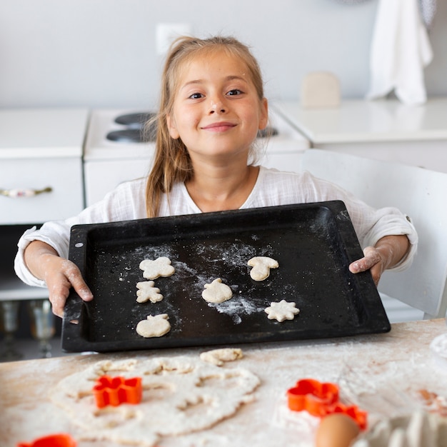 Free photo adorable little girl holding tray with dough