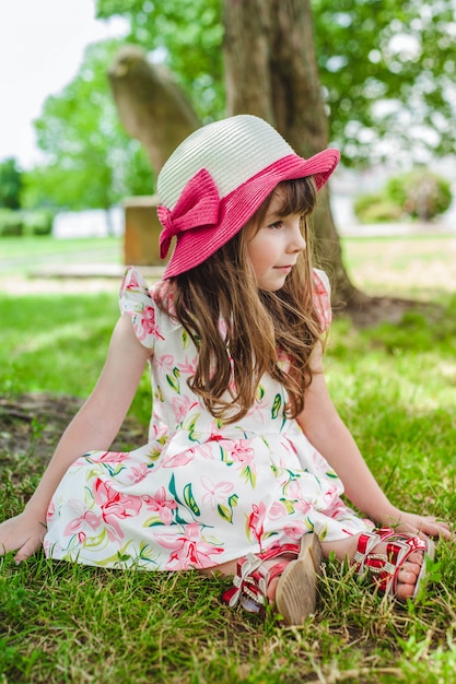 Adorable little girl sitting on the floor in a park with a hat