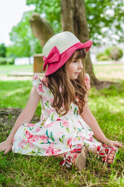 Adorable little girl sitting on the floor in a park with a hat