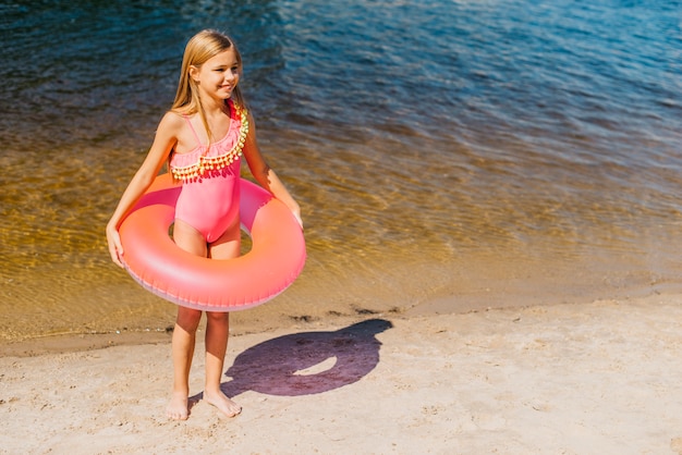 Очаровательная маленькая девочка с ярким кольцом для плавания на берегу моря