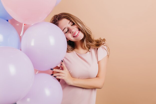 Adorable long-haired woman standing with eyes closed and holding party balloons