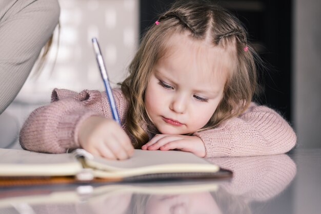 Adorable preschool girl drawing with pen at table