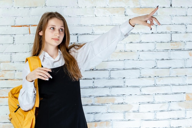 Adorabile studentessa si erge su sfondo bianco e indica la mano da parte