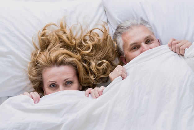 Free photo adorable senior couple under bed sheets