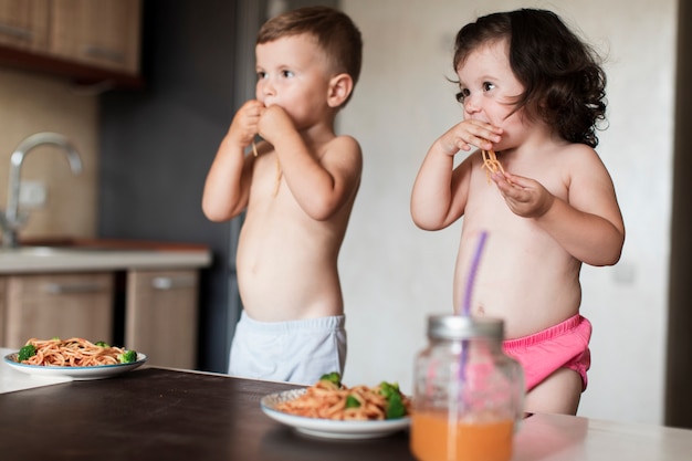 Adorable siblings eating spaghetti