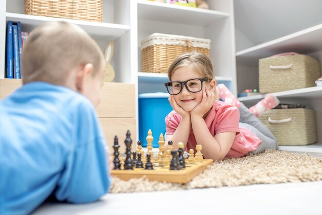 Adorable siblings  lying on the ground and playing chess with each other