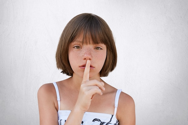 Adorable small kid showing silent sign asking to be noiseless as her little