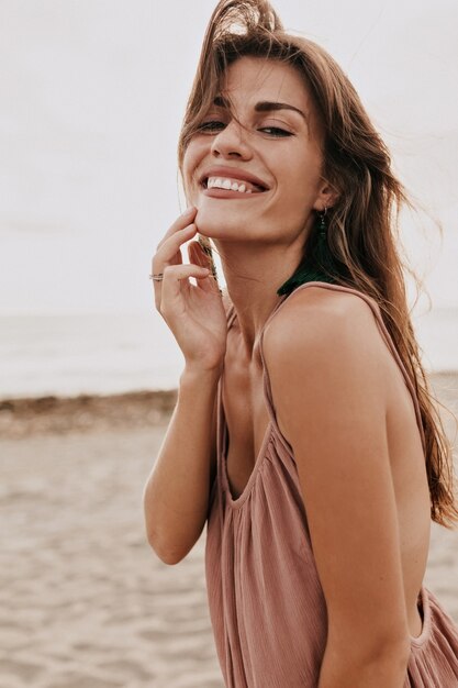日光の下で海のそばの砂浜のカメラで笑っている愛らしい笑顔の女性