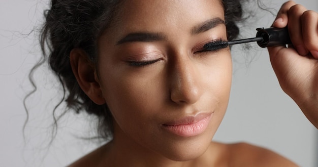 Adorable teenage Middle Eastern girl with great skin applying mascara to her long lashes on white background