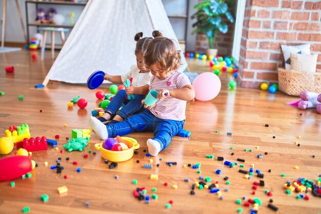 Adorable toddlers playing meals using plastic food and cutlery toy at kindergarten