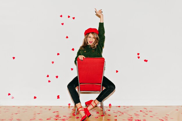 Adorable white woman sitting on red chair with hand up