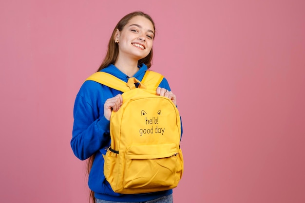 Adorable woman in blue blouse smiling at camera while carrying funny knapsack vice versa indoors