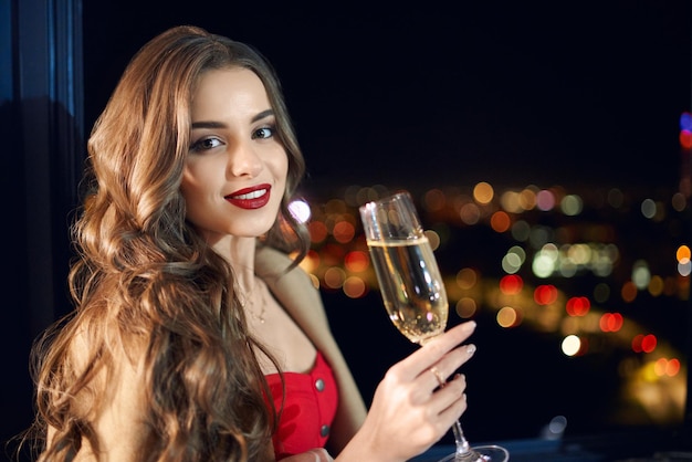 Adorabile donna in abito rosso in posa con un bicchiere di champagne Foto Gratuite