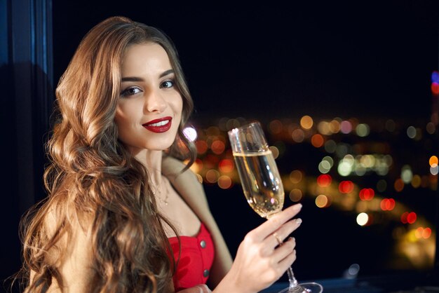 Очаровательная женщина в красном платье позирует с бокалом шампанского