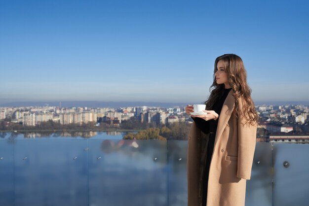 Очаровательная женщина, стоящая на балконе с чашкой кофе