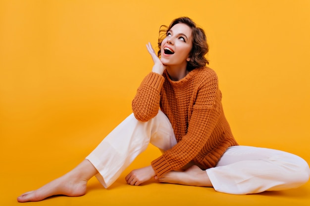 Adorable woman with dreamy face expression looking up while sitting on the floor