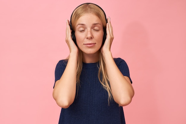 주근깨가 눈을 유지하는 사랑스러운 젊은 백인 여자는 무선 헤드폰을 사용하여 그녀가 좋아하는 음악 아티스트의 새 앨범을 즐기고 폐쇄