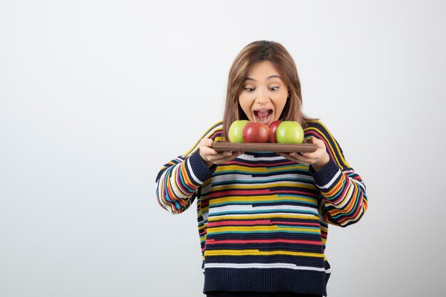 Free photo adorable young girl in casual clothes eating bunch of apples.